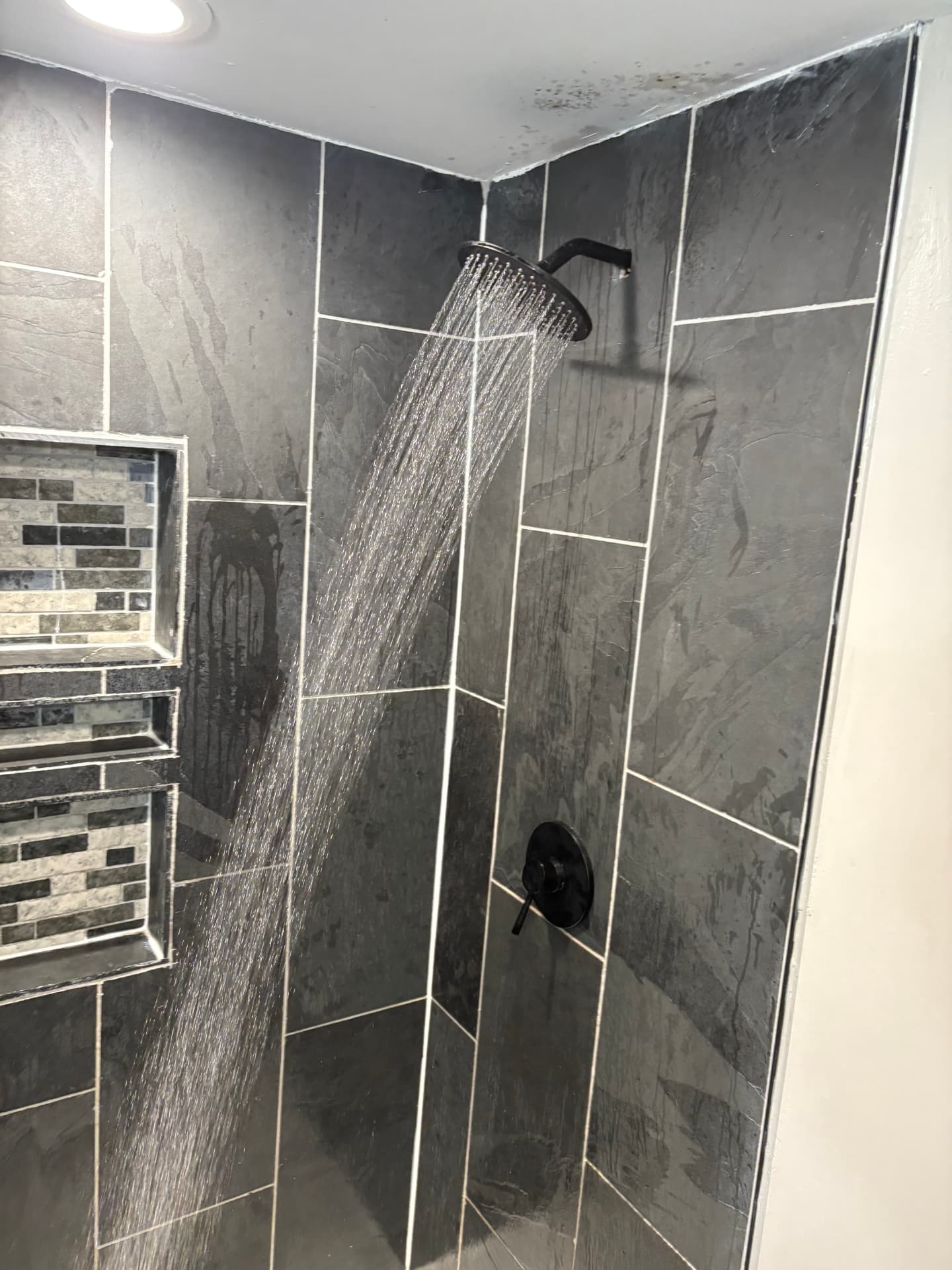Black rain shower head running water in a renovated slate tile shower in Columbia, MD — ProStream Plumbing