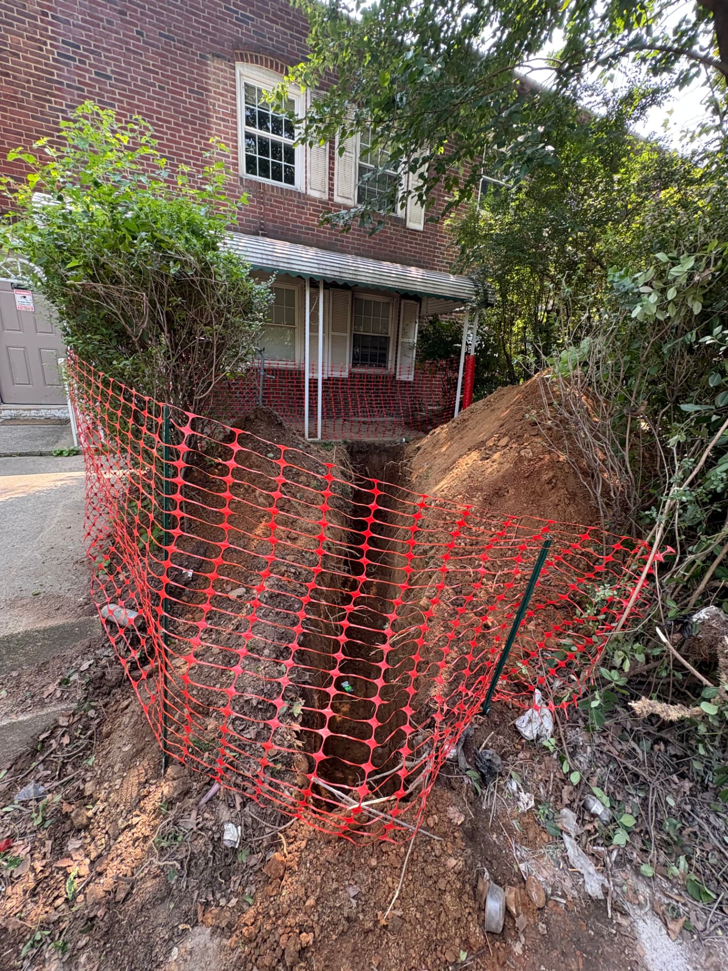 Deep sewer line replacement trench protected by safety fencing at a brick rowhome in Baltimore, MD — ProStream Plumbing