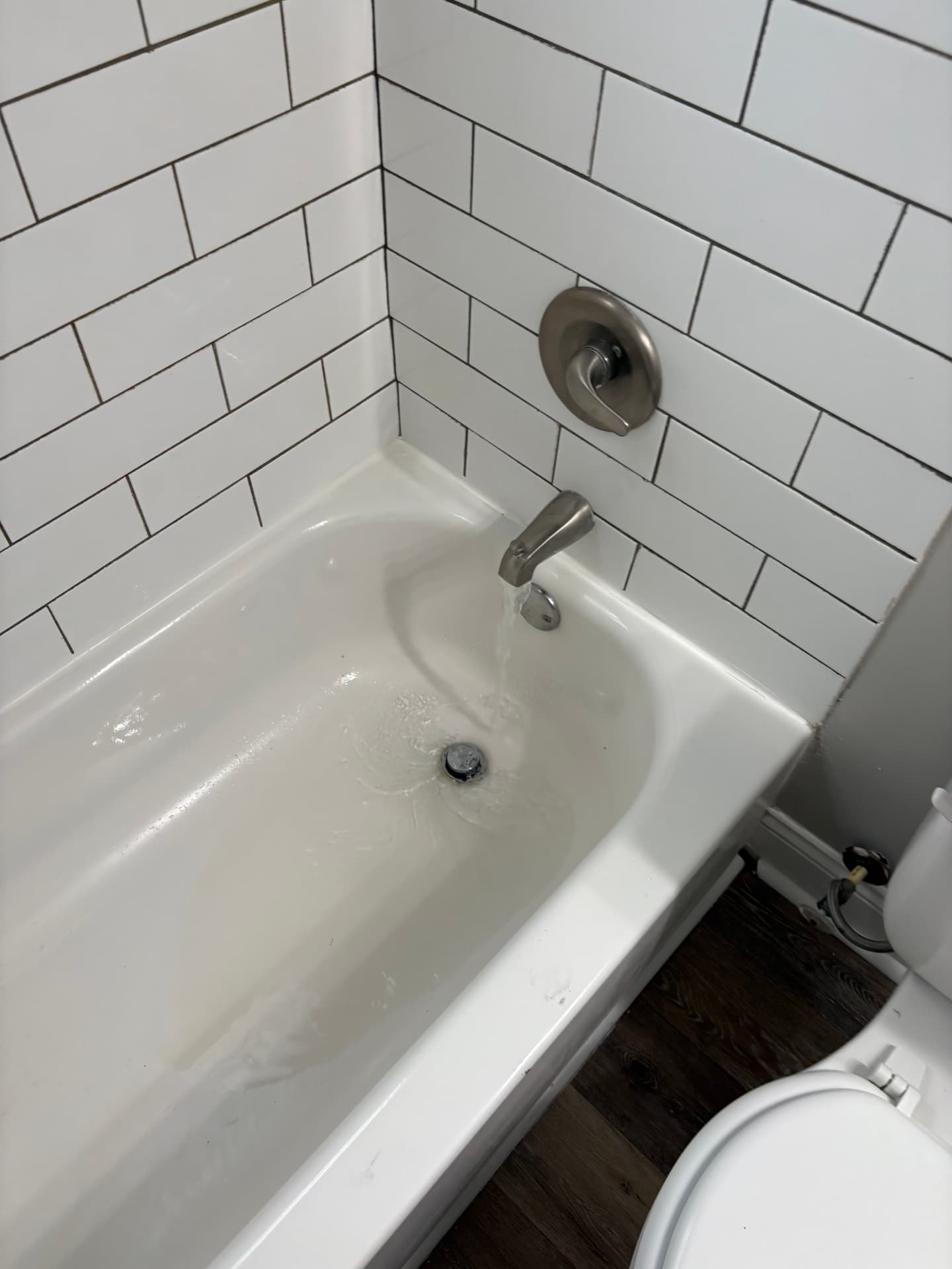 Bathtub with water running from a new brushed nickel spout in a subway tile surround in Baltimore, MD — ProStream Plumbing